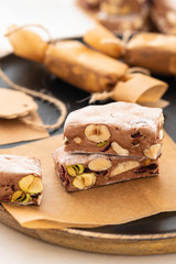 A variety of different nutty nougat in dark chocolate with roasted hazelnuts cut open to show the nougat mix on a wooden board . Copy space.