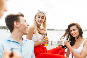 A company of good-looking friends laughing and drinking yellow cocktails and socialising in the nice cafe next to the river. Cheers. Entertainment, having good time. River is in the background.