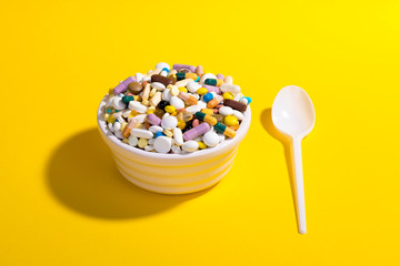 Bowl full of colorful pills on yellow background with plastic spoon. Creative composition. - Powered by Adobe