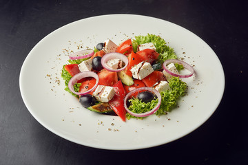 Greek salad of fresh cucumber, tomato, sweet pepper, lettuce, red onion, feta cheese and olives with olive oil on white plate