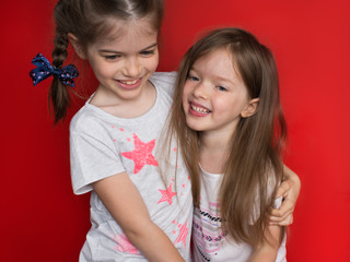 Happy funny girl twins sisters hugging and laughing, red background