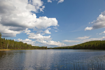 Beautiful volumetric clouds on a sunny day over a quiet forest lake