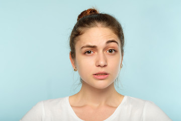 bewildered dubious distrustful girl with raised eyebrow. young beautiful woman with a hair bun on blue background. emotional facial expression.