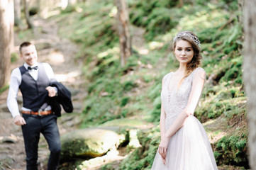 Attractive couple newlyweds, happy and joyful moment. Man and woman in festive clothes sit on the stones near the wedding decoration in boho style. Ceremony outdoors.