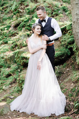 Attractive couple newlyweds, happy and joyful moment. Man and woman in festive clothes sit on the stones near the wedding decoration in boho style. Ceremony outdoors.