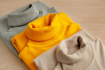 Three turtlenecks of different colors. Three turtleneck classic style for the autumn and winter seasons. Warm clothing from knitwear on a wooden background. Women's fashion.