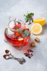 Glass teapot with tea, mint and lemon on grey table with copy space