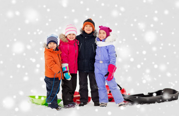 childhood, friendship and season concept - group of happy little kids with sleds hugging in winter