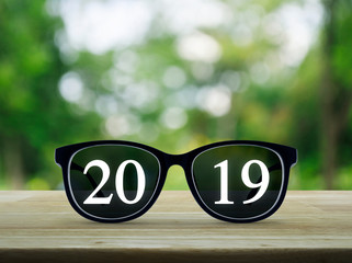 2019 white text with black eye glasses on wooden table over blur green tree in park, Business vision, Happy new year 2019 concept