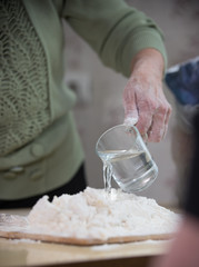 An old lady making little pies. Making dough with pouring the water