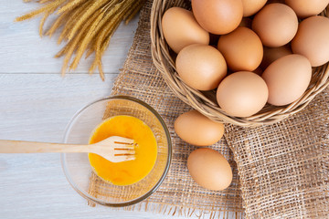 Eggs in a wooden basket and yolk in a bowl on a white wooden table.