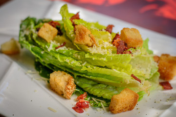 caesar's salad with bacon bits and crispy croutons on white porcelain plate