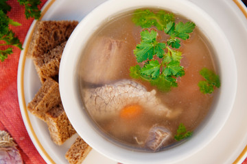 Clear beef broth, bouillon in white bowl and vegetables on wooden table. Rustic style. Top view.