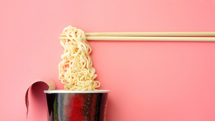 Instant noodles cup and chopsticks on a pink background. - 229893108