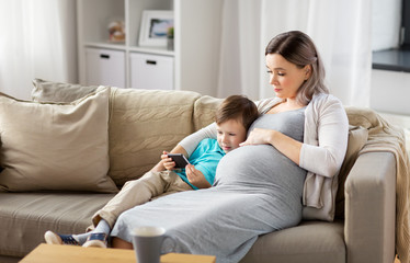 family, technology and pregnancy concept - happy pregnant mother and little son with smartphone at home
