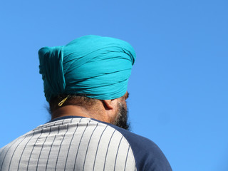 Bearded Indian sikh in a cyan turban on a background of clear blue sky, rear view. Man wearing...