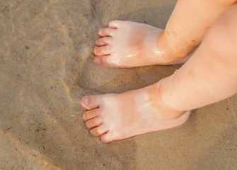 Toddler baby doing his first steps on the beach. Bare feet baby staying on the sand near the bank in sunny day. Summertime holidays concept. Top view. Copy space