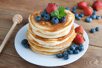 American pancakes or fritters served with strawberry and blueberry jam, delicious dessert for breakfast, rustic style, wooden background.