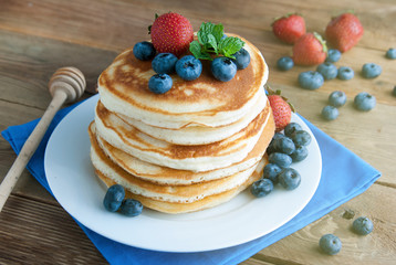 American pancakes or fritters served with strawberry and blueberry jam, delicious dessert for breakfast, rustic style, wooden background.