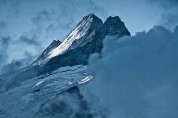 Closeup of summit Nässihorn Grindelwald with glacier and snow during sunrise framed by clouds