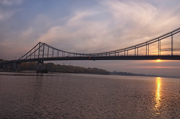 Wide angle landscape panorama of Dnipro River, embankment and Pedestrian Bridge. Colorful vibrant sky, sun reflected in the water. Foggy autumn morning during sunrise. Kyiv, Ukraine