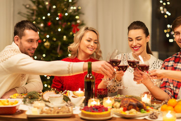 holidays and celebration concept - happy friends having christmas dinner at home, drinking red wine and clinking glasses