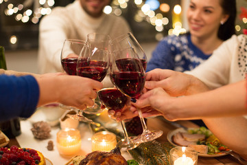 holidays and celebration concept - close up of happy friends having christmas dinner at home, drinking red wine and clinking glasses