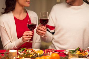 holidays, family and celebration concept - close up of happy couple having christmas dinner at home and drinking red wine