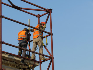 Welders working on the construction site against the clear blue sky. Construction workers on scaffolding, welding work