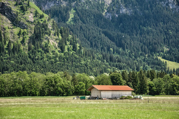 An old bavarian farm in Bavarian Alps, south Bavaria, Germany. Spring or summer sunny day. Mountains on a background. Typical peaceful bavarian landscape.