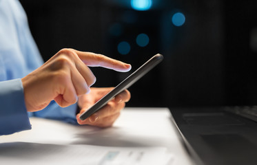 business, deadline and technology concept - close up of businesswoman hands with smartphone at night office