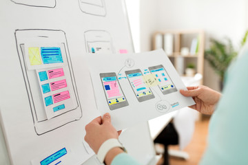 technology, user interface design and people concept - hand of ui designer or developer with smartphone app templates and flip chart working at office
