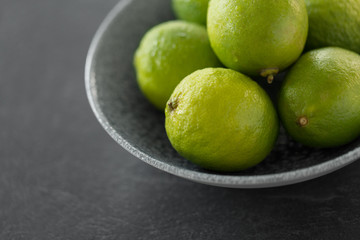 food, healthy eating and vegetarian concept - close up of whole limes in bowl on slate table top
