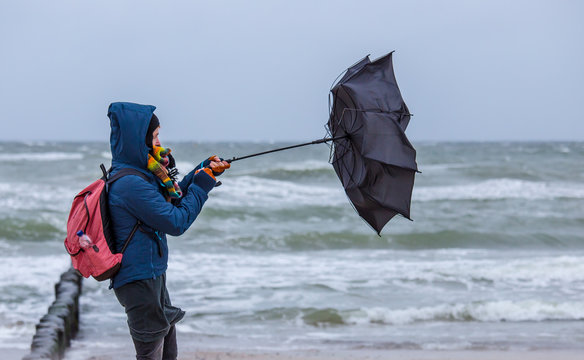 strong wind destroys a woman's umbrella during a beach walk
