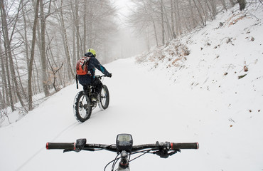 man riding electric bicycle, e-bike, ebike, on snowy road, during snow storm, handlebars and display of the second bike, high mountain, end of winter, spring, cold, alps, adventure, Piedmont, Italy