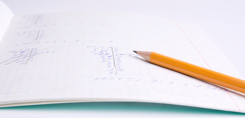 The pencil is on the notebook of the student. Close up.