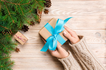 female hands hold wrapping christmas gift box with blue ribbon on brown wooden table. Top view