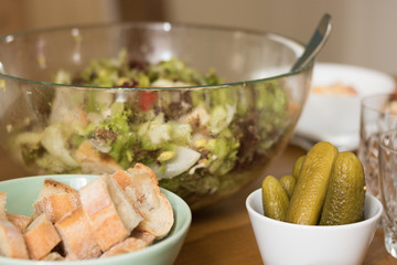 Pickles, bread and a big bowl of Caesar salad are on a table.
