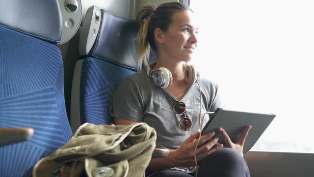 Young woman travelling by train with tablet and headphones                              