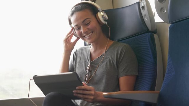 Young woman travelling on train with tablet and headphones                              