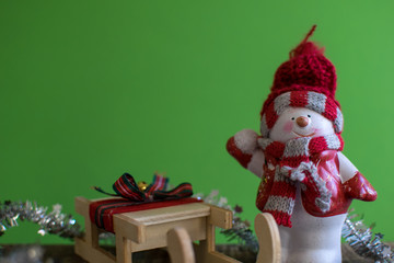 Closeup of snowman with a red scarf and white scarf throwing a snowball and a snowsled