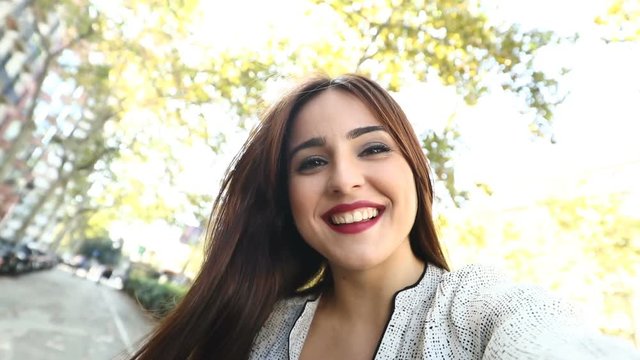 Happy woman holding a camera taking selfies in the street recorded in slow motion