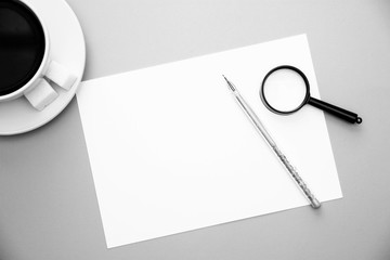 pen white paper magnifier and coffee Cup on yellow background with copy space top view black and white image