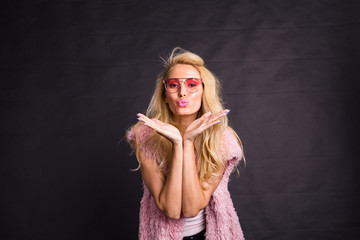 Fashion and beauty concept - beautiful blond model send kisses over dark background
