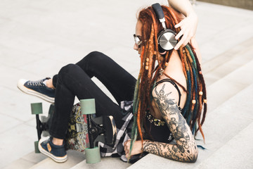 young girl with tattoo and dreadlocks listening to music while sitting on the steps