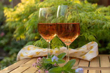 Two cold rose wine glasses served on outdoor terrace in garden with flowers in sunny day