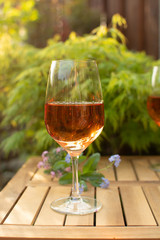 One cold rose wine glass served on outdoor terrace in garden with flowers
