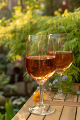 Two cold rose wine glasses served on outdoor terrace in garden with flowers in sunny day