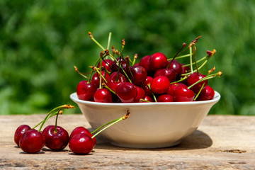 Bowl with fresh cherry on rustic wooden table outdoor