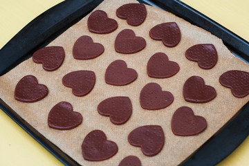 Uncooked heart shaped cookies on baking papper, raw dough and heart shaped cookie cutter. top view.